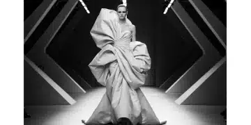 Modelo de Alta Costura exhibiendo un vestido con volúmenes esculturales y drapeados intrincados en una pasarela futurista.