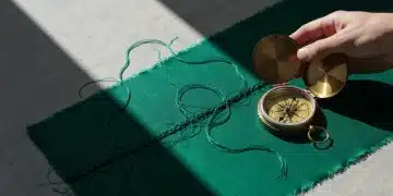 A hand unraveling emerald green silk next to a tarnished brass compass, symbolizing fashion's shift towards transparency and circularity.